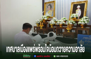ชายสวมเสื้อขาวนั่งลงนามถวายความอาลัยหน้าโต๊ะหมู่บูชาที่มีพระบรมฉายาลักษณ์และพานพุ่มดอกไม้สีขาว