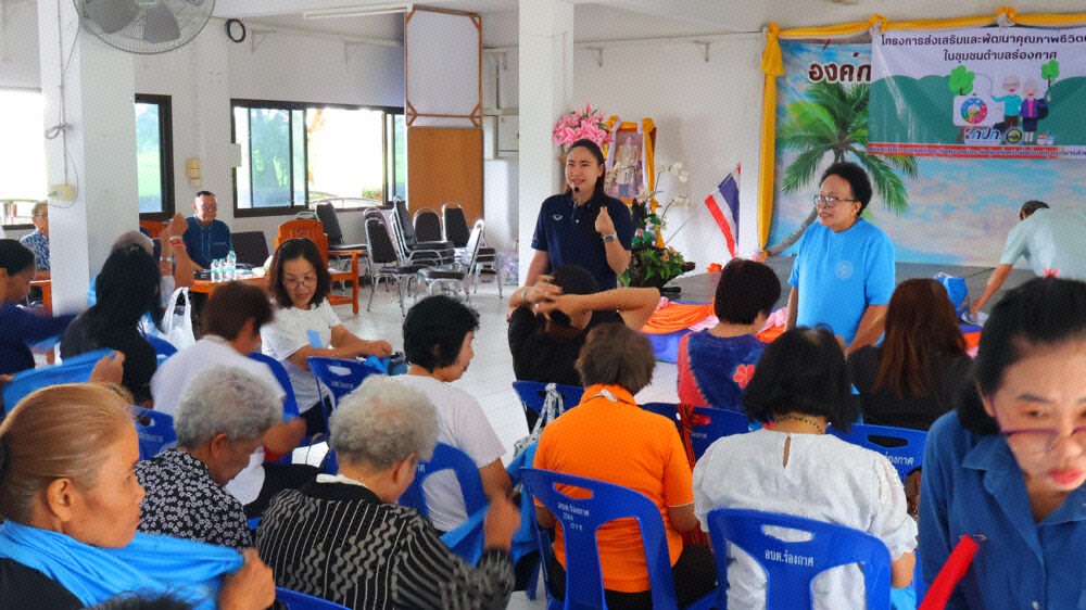 การประชุมกลุ่มผู้สูงอายุในชุมชน มีวิทยากรยืนบรรยายอยู่ด้านหน้าห้องประชุมที่มีผู้เข้าร่วมรับฟังจำนวนมาก