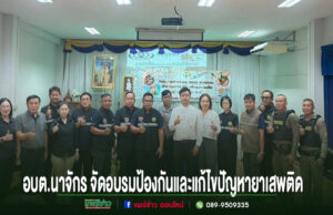 กลุ่มคนยืนเรียงแถวถ่ายรูปหมู่ในห้องประชุม มีป้ายข้อความภาษาไทยด้านล่างภาพ
