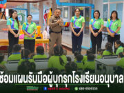 ตำรวจและครูกำลังบรรยายให้ความรู้แก่เด็กนักเรียนอนุบาลที่นั่งฟังอยู่บนเก้าอี้และบนพื้นห้องเรียน