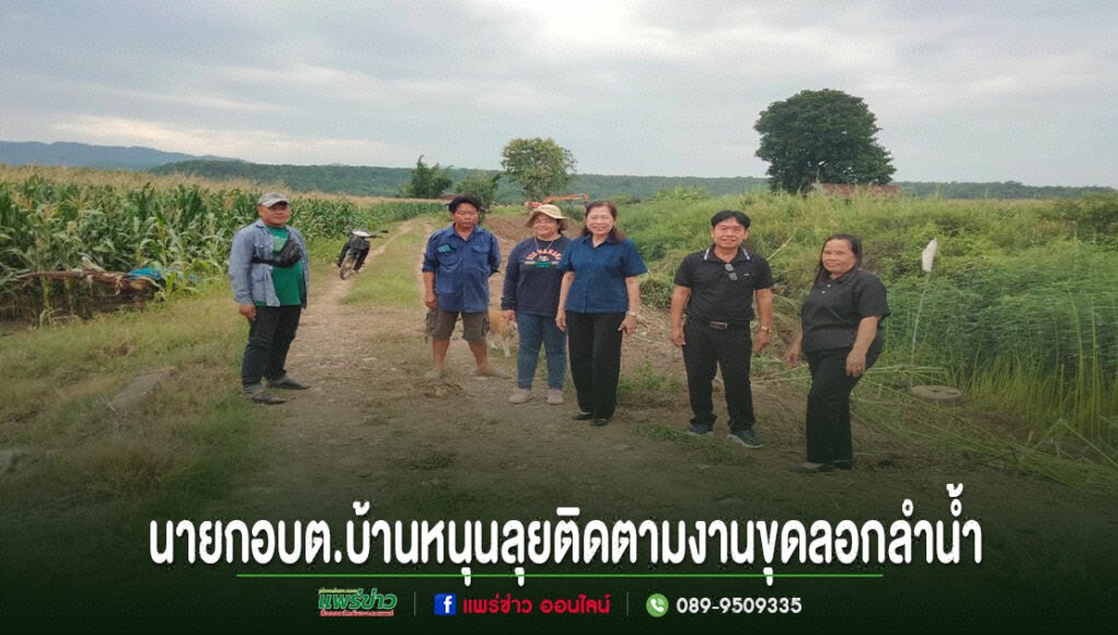 กลุ่มคนยืนถ่ายรูปบนถนนลูกรังกลางทุ่งนา มีข้อความภาษาไทยด้านล่างภาพ