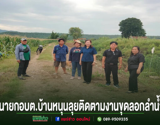 อบต.บ้านหนุนลุยติดตามงานขุดลอกลำน้ำขอบคุณ อบจ.แพร่ สนับสนุนรถแม็คโคร 2 คัน กลุ่มคนยืนถ่ายรูปบนถนนลูกรังกลางทุ่งนา มีข้อความภาษาไทยด้านล่างภาพ