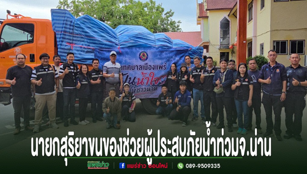 กลุ่มคนยืนถ่ายรูปหน้าขบวนรถบรรทุกสิ่งของช่วยเหลือผู้ประสบภัยน้ำท่วมจังหวัดน่าน