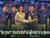 กลุ่มคนยืนเรียงแถวหน้ากระดานบนเวที โดยมีหญิงสาวสวมเสื้อสีครีมยื่นซองจดหมายให้ชายสวมเสื้อโปโลสีน้ำเงินด้านข้าง