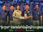 กลุ่มคนยืนเรียงแถวหน้ากระดานบนเวที โดยมีหญิงสาวสวมเสื้อสีครีมยื่นซองจดหมายให้ชายสวมเสื้อโปโลสีน้ำเงินด้านข้าง