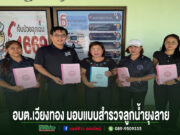 กลุ่มคน 5 คนยืนถือสมุดรายงานหน้าป้ายประชาสัมพันธ์ อบต.เวียงทอง มอบแบบสำรวจลูกน้ำยุงลาย