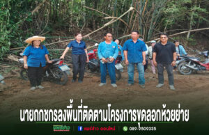 กชกร เกยงค์ นายกอบต.บ้านหนุน ลงพื้นที่ติดตามโครงการขุดลอกห้วยย่าย เพิ่มประสิทธิภาพการระบายน้ำในชุมชน กลุ่มคนยืนถ่ายรูปบนถนนดินลูกรัง มีป้ายข้อความภาษาไทยด้านล่างภาพ