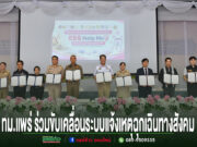 กลุ่มคนยืนเรียงแถวถือเอกสารความร่วมมือระบบแจ้งเหตุฉุกเฉินทางสังคม ESS Help Me บนเวทีที่มีดอกไม้ประดับด้านหน้า
