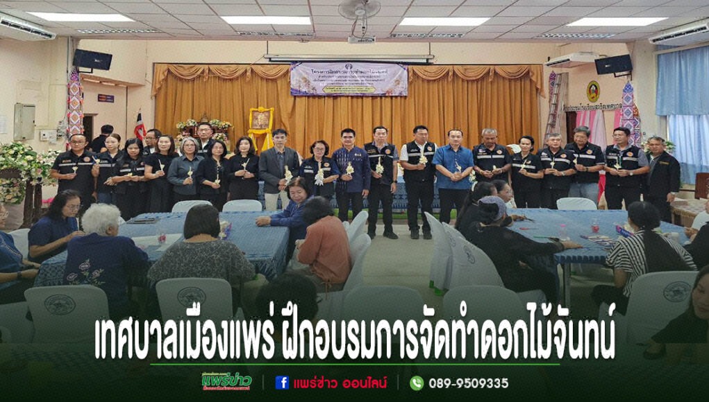 กลุ่มคนยืนเข้าแถวถือดอกไม้จันทน์อยู่หน้าเวที และมีผู้เข้าฝึกอบรมการทำดอกไม้จันทน์นั่งตามโต๊ะ