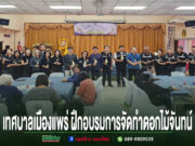 กลุ่มคนยืนเข้าแถวถือดอกไม้จันทน์อยู่หน้าเวที และมีผู้เข้าฝึกอบรมการทำดอกไม้จันทน์นั่งตามโต๊ะ