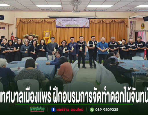 กลุ่มคนยืนเข้าแถวถือดอกไม้จันทน์อยู่หน้าเวที และมีผู้เข้าฝึกอบรมการทำดอกไม้จันทน์นั่งตามโต๊ะ